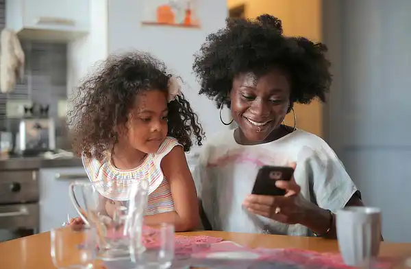 Mamá feliz con sus hijos desayunando y usando app Elfester rediseñada.